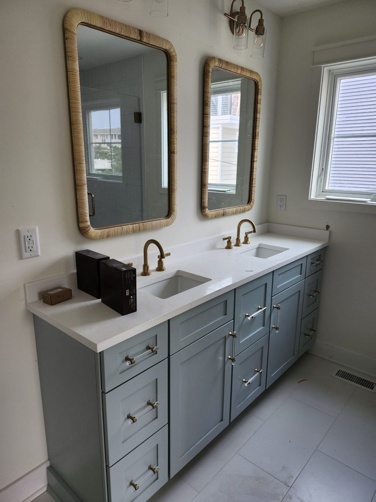 Custom blue-gray double vanity with quartz counters, brass fixtures, and rattan-framed mirrors