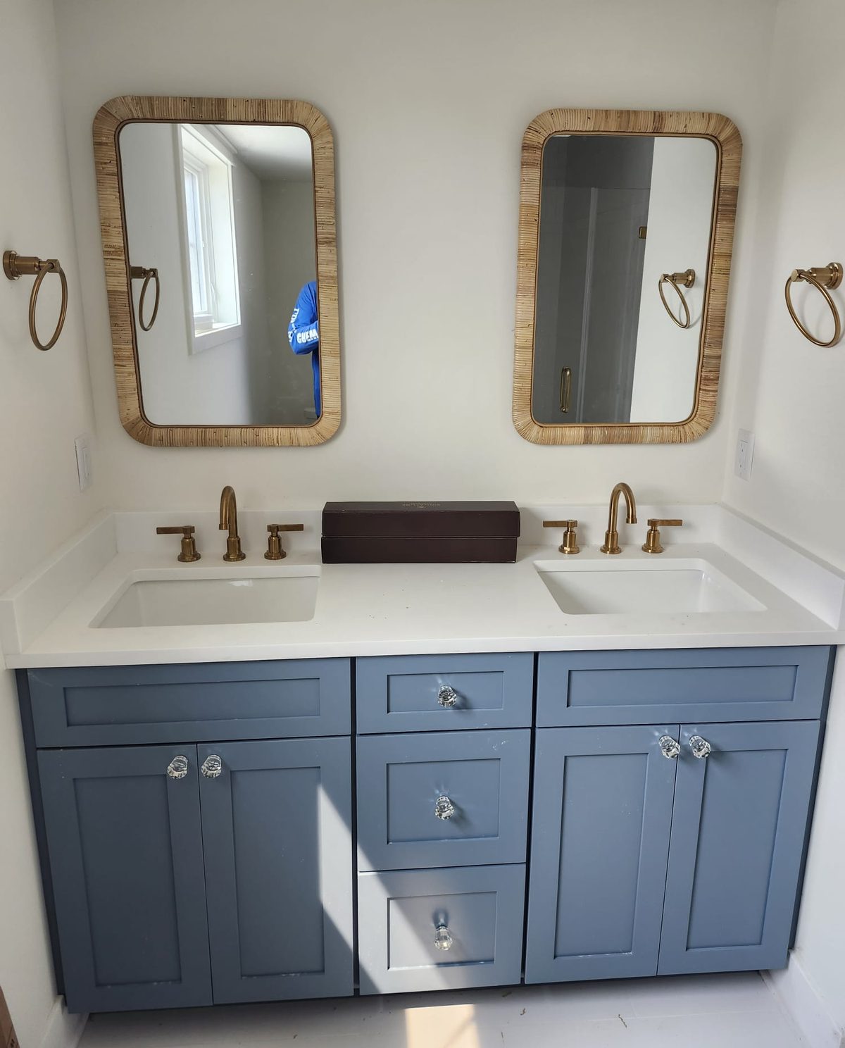 Finished double vanity by FMA Constructions with rattan mirrors, brushed brass faucets, and white quartz countertops